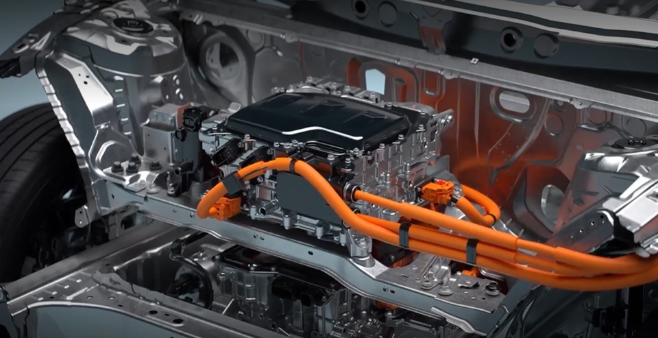 Close-up of a Toyota hybrid or electric powertrain showing the battery unit with high-voltage orange cables exposed inside the vehicle frame.