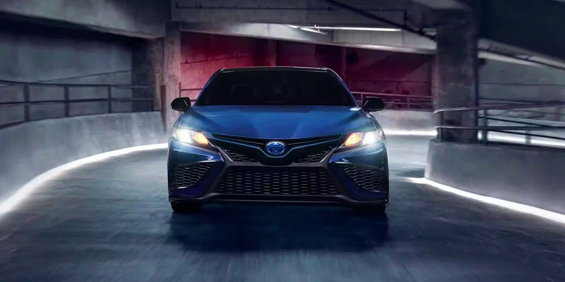 Front view of a blue Toyota Camry Hybrid in a modern parking garage with dramatic lighting.