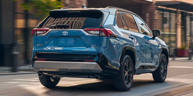 Blue Toyota RAV4 Hybrid on city street, rear view.